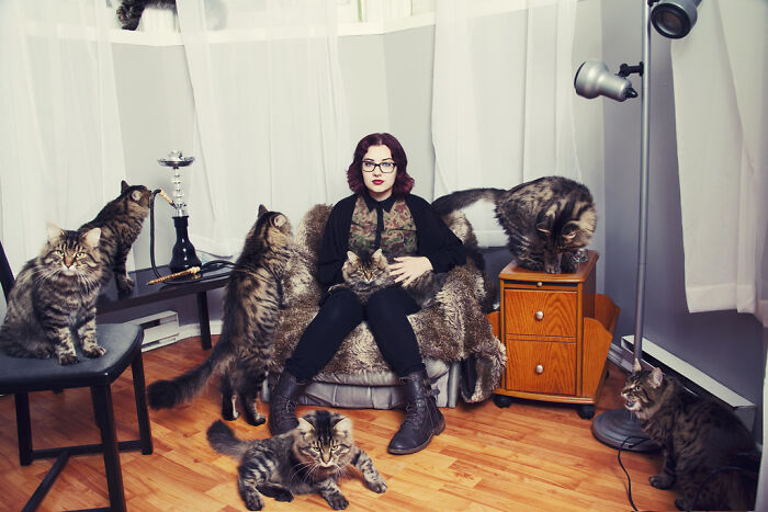 Woman surrounded by multiple cats indoors, showcasing the best of cat photography with adorable cat pics.