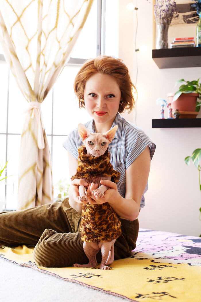 Woman holding a hairless cat wearing a leopard print outfit in a bright room, showcasing the best of cat photography.
