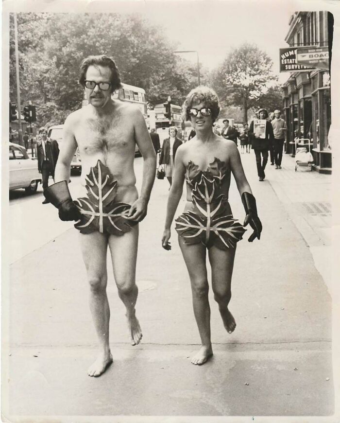 Vintage photo of a man and woman walking barefoot in leaf costumes on a city street, showcasing mesmerizing history.