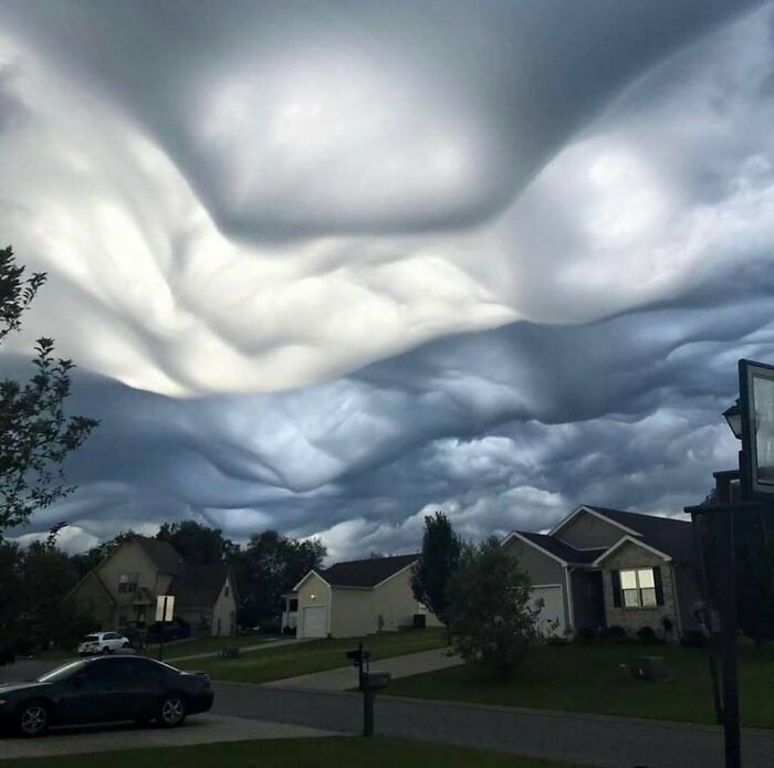 Unsettling yet fascinating empty spaces shown by surreal, undulating cloud formations over a quiet suburban neighborhood at dusk.