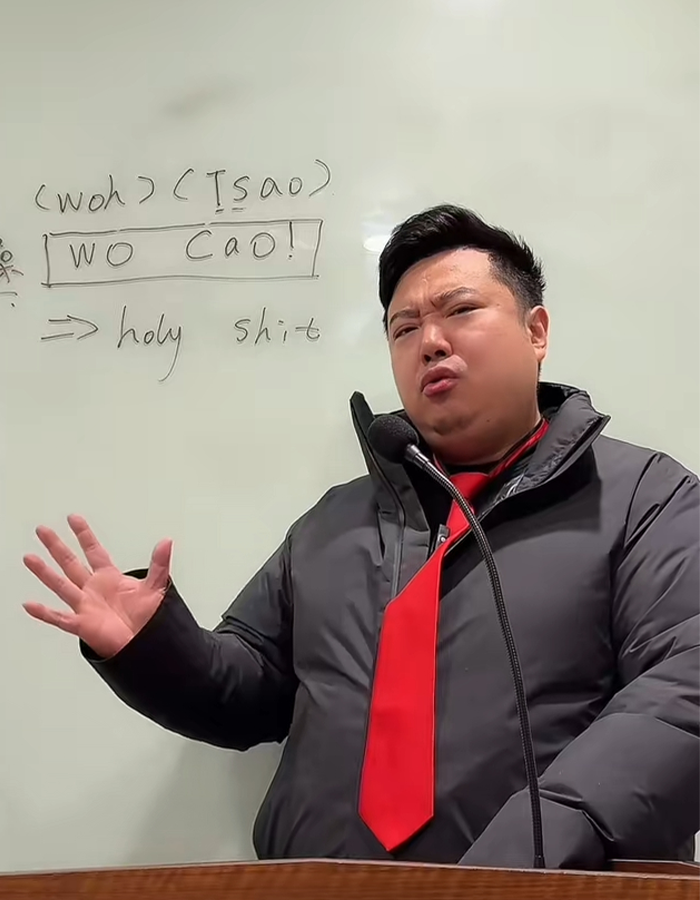 Chinese TikToker imitating U.S. President's speech wearing a black jacket and red tie in front of a whiteboard.