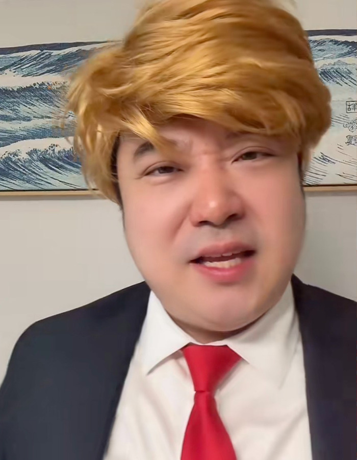 Chinese TikToker dressed as U.S. president with blond wig and red tie, performing viral impression in front of wave artwork.