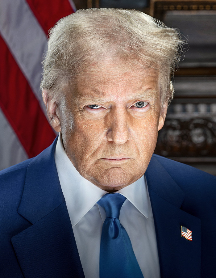 Close-up of a man resembling Donald Trump wearing a blue suit and tie with an American flag pin and background.