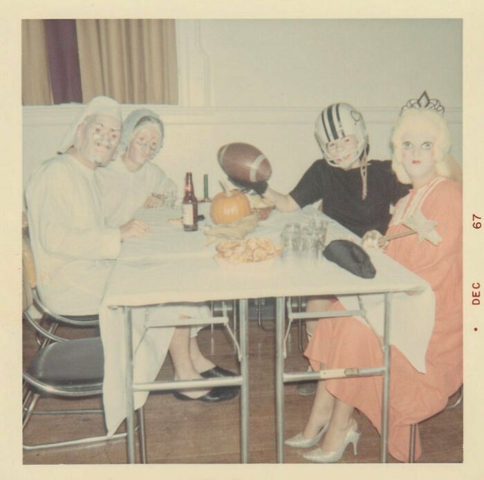 Vintage photo of people in Halloween costumes gathered around a table with a pumpkin and football, capturing vintage moments.