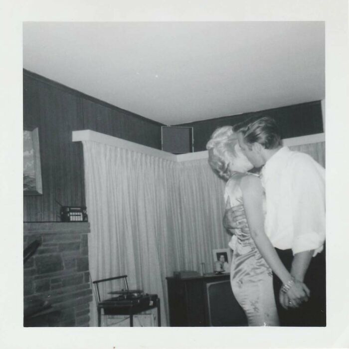 Black and white vintage photo of a couple kissing passionately in a living room, showcasing intimate moments from history.