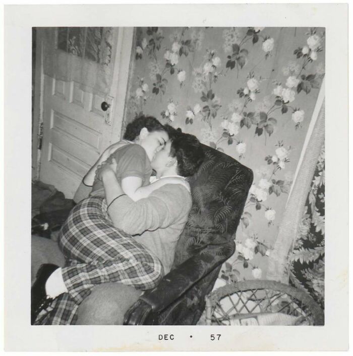 Vintage photo from 1957 showing a couple embracing on a floral wallpaper background in a cozy room.
