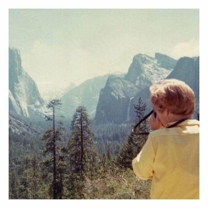Child in a yellow jacket taking a photo in a forested mountain landscape in a vintage photo capturing history.