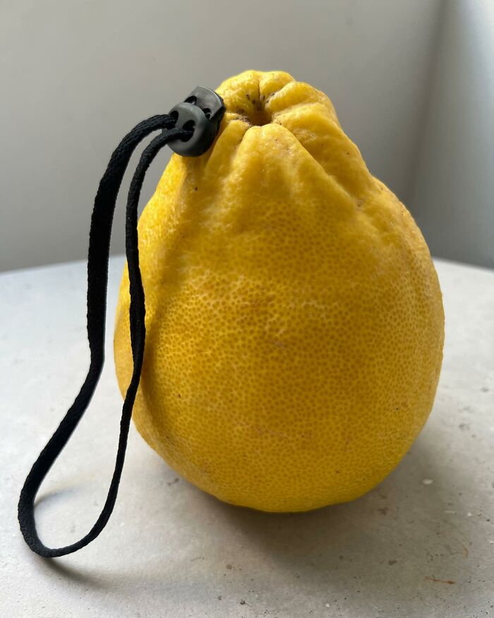 Yellow textured fruit resembling a photo manipulation collage featuring an attached black cord and plastic toggle on a white surface.