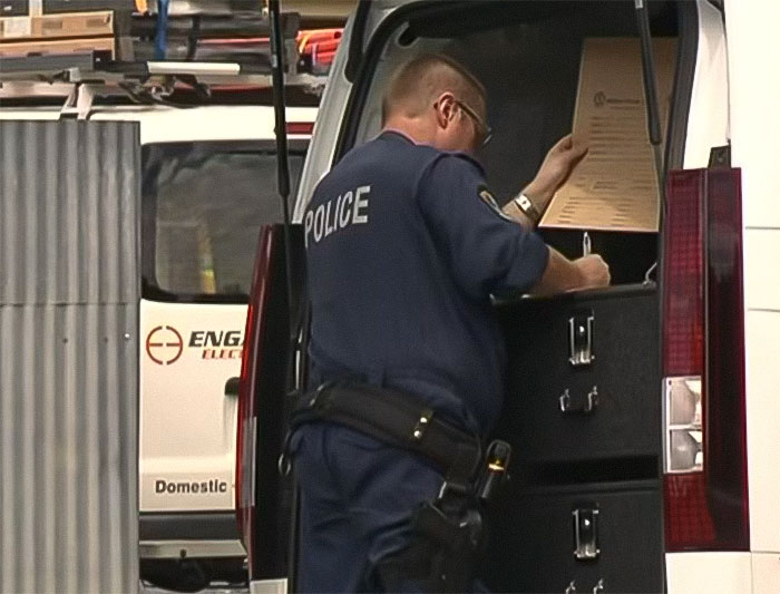 Police officer investigating incident, writing notes at the back of a police van related to woman sets childhood male friend on fire case.