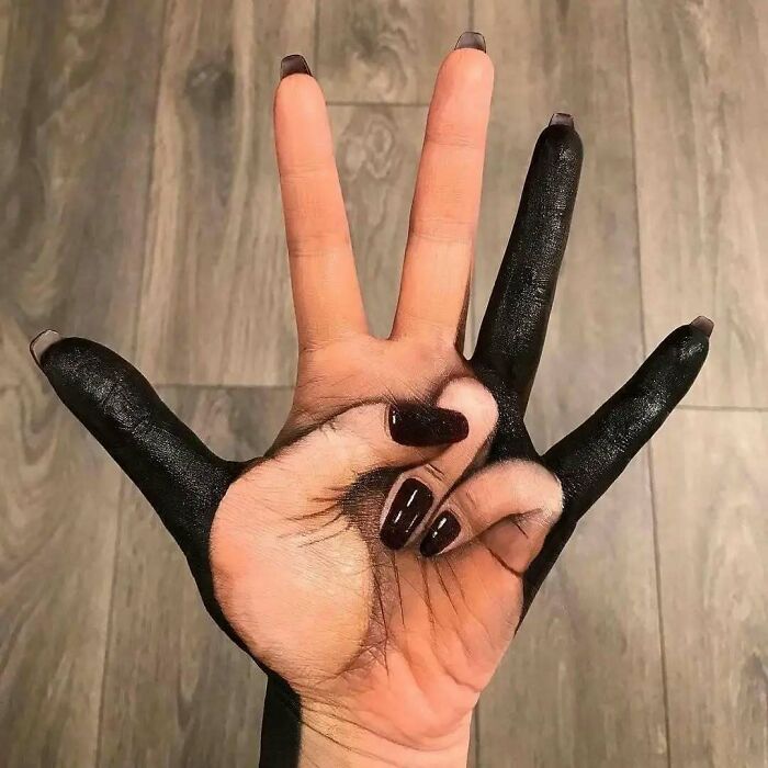 Mano con tatuaje creativo que combina espacio negativo y pintura negra, ejemplo de tatuajes que van de lo gracioso a lo terrible.