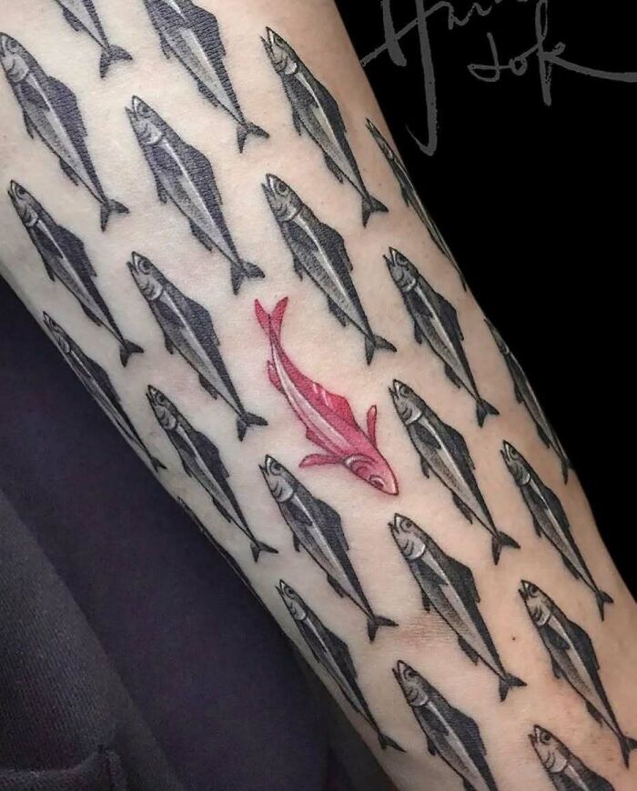 Tatuaje de varios peces negros con un pez rosa que destaca, ejemplo original y creativo en tatuajes únicos.