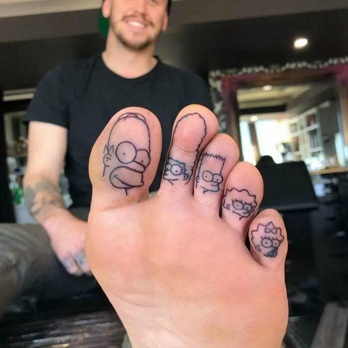 Funny and interesting tattoos of cartoon characters inked on each toe with a blurred smiling person in the background.
