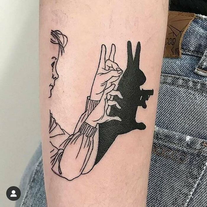 Tatuaje creativo de sombra con manos que forman una figura divertida en el brazo, ejemplo de tatuajes de personas.