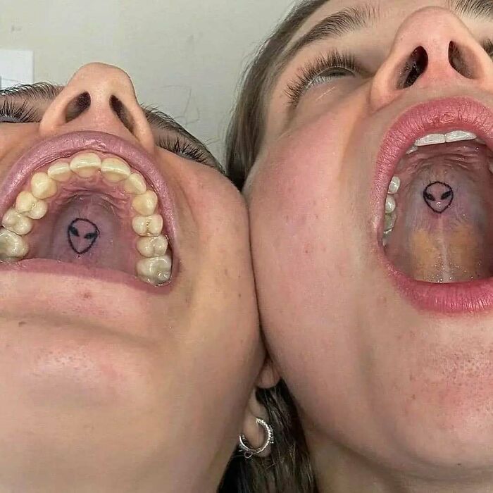 Two people showing matching alien face tattoos on the roof of their mouths in a funny and interesting tattoo idea.