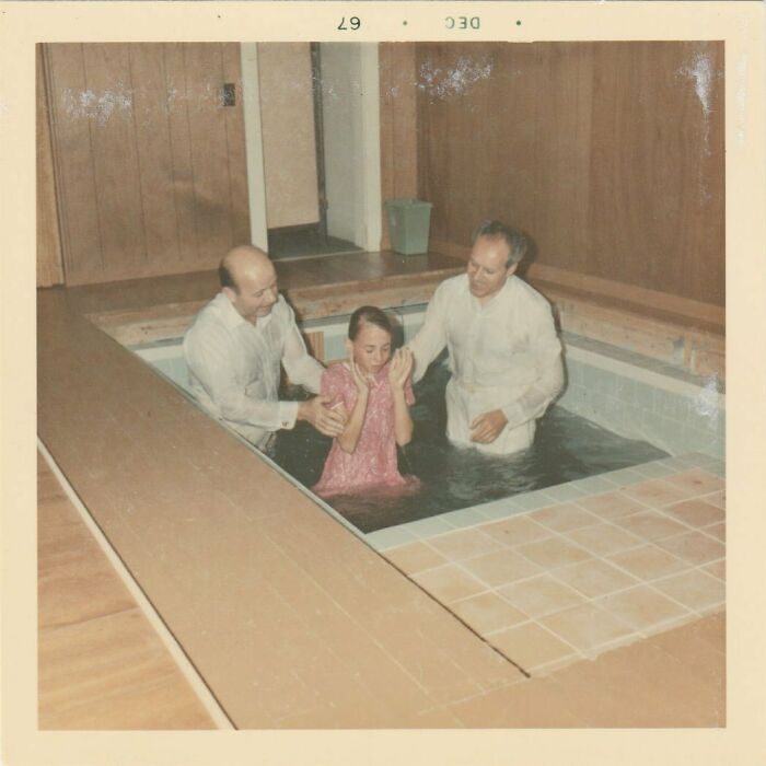 Vintage photo of a religious baptism ceremony with two men and a young girl in an indoor pool.