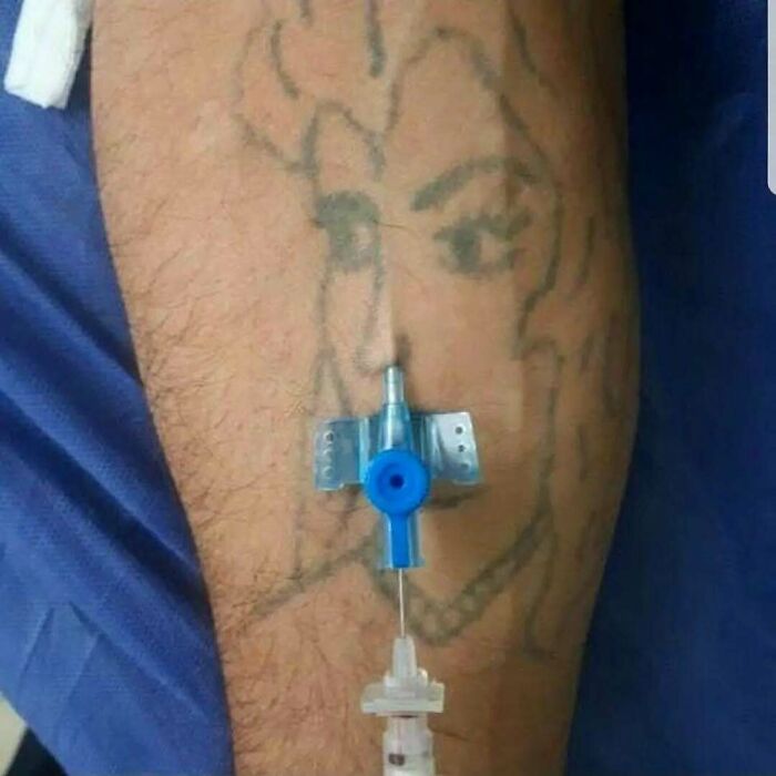 Arm with tattoo aligned to create an uncanny effect with medical IV needle inserted into vein during treatment.