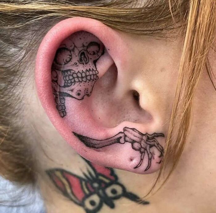 Tatuaje de calavera y huesos en la oreja, muestra creatividad y estilo único en personas con tatuajes llamativos y variados.