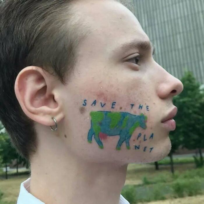 Young man with a colorful face tattoo of a cow and the words save the planet, showcasing funny and interesting tattoos.