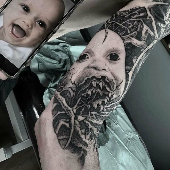 Tattoo of a distorted baby face with sharp teeth covering an arm, creating a funny and interesting tattoo design.
