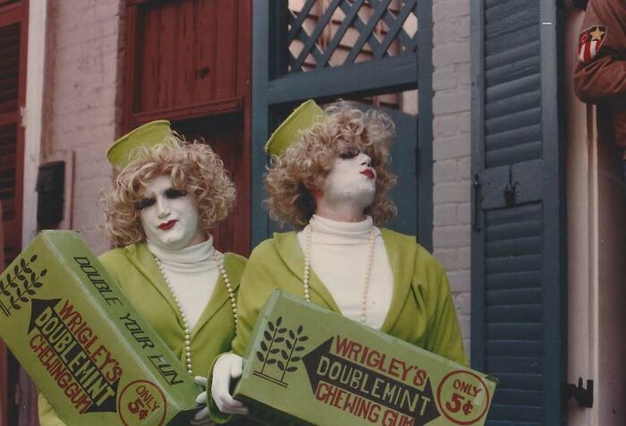 Two people dressed in vintage costumes holding Wrigley's Doublemint chewing gum boxes in an old street setting.