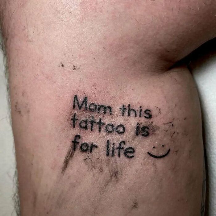 Close-up of a funny and bad tattoo on skin that reads Mom this tattoo is for life with a smiley face.