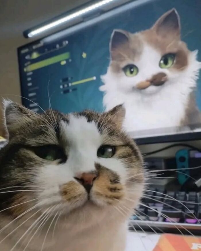 Tabby cat posing in front of a computer screen showing a digital drawing of a quirky cat with green eyes and a mustache.