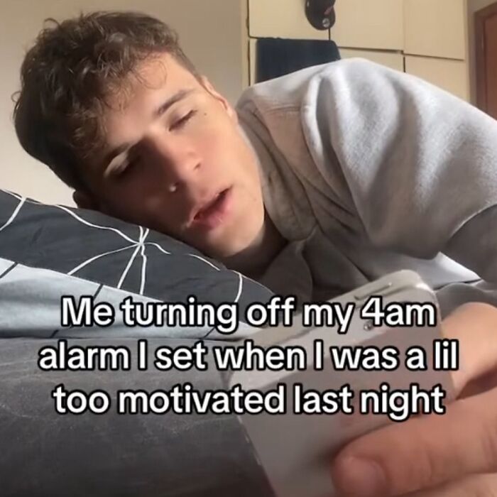 Young man lying in bed turning off phone alarm, relatable and silly meme shared on IG page with spicy humor.