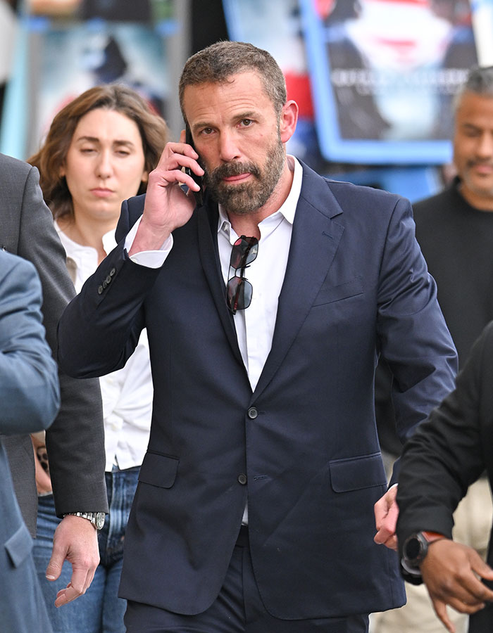 Man in a dark suit talking on phone, surrounded by people, related to Netflix star viral x-rated wardrobe malfunction news.