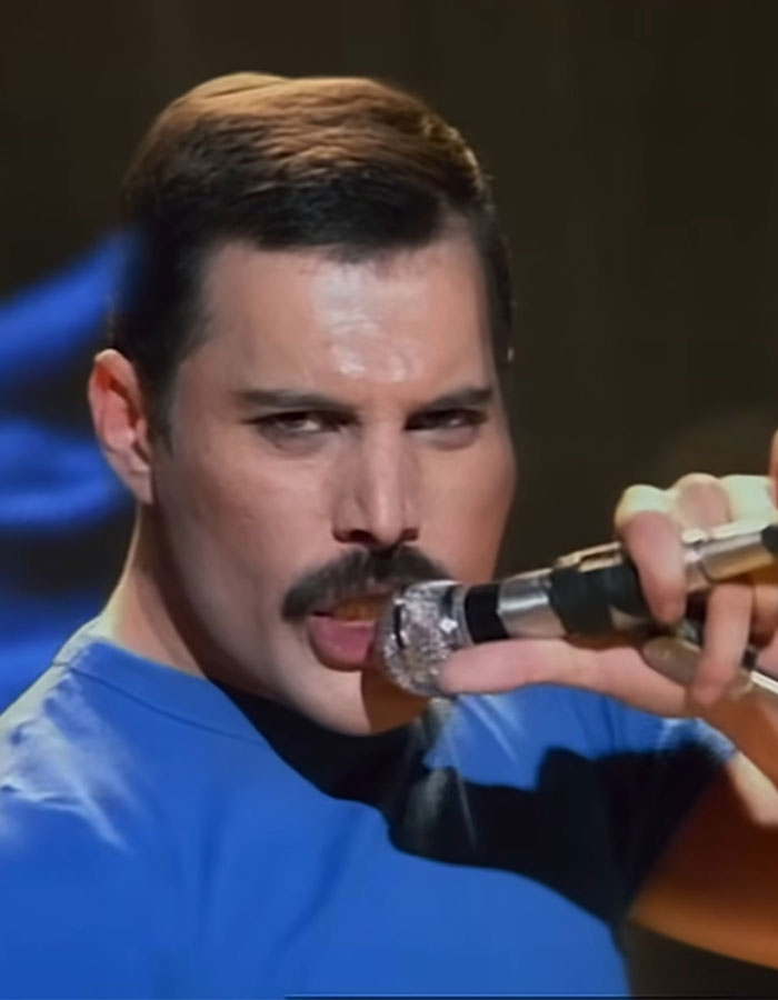Close-up of Freddie Mercury performing on stage holding a sparkling microphone, highlighting his iconic mustache and intense expression.