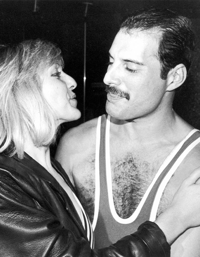 Freddie Mercury in a close moment with a woman, showcasing his signature mustache and distinctive style in a candid black and white photo.