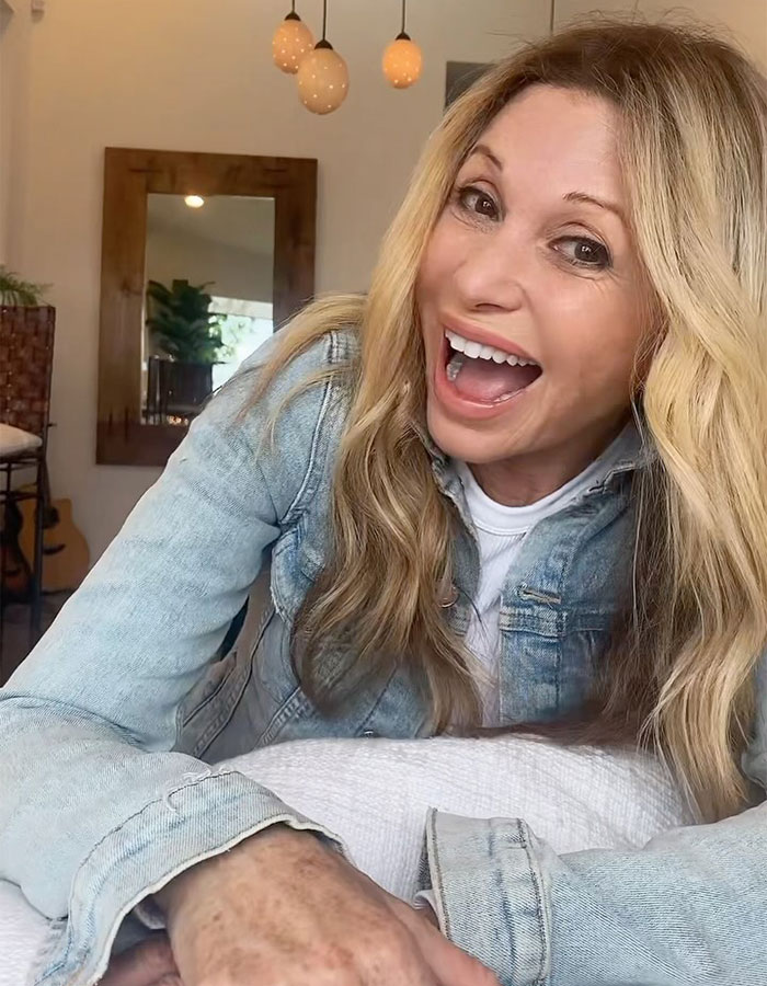 63YO Friends star known for Smelly Cat smiling with a youthful glow, wearing a denim jacket indoors.