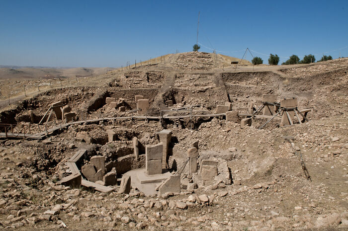 Ancient archeological discovery site with stone pillars and excavation areas under a clear blue sky.