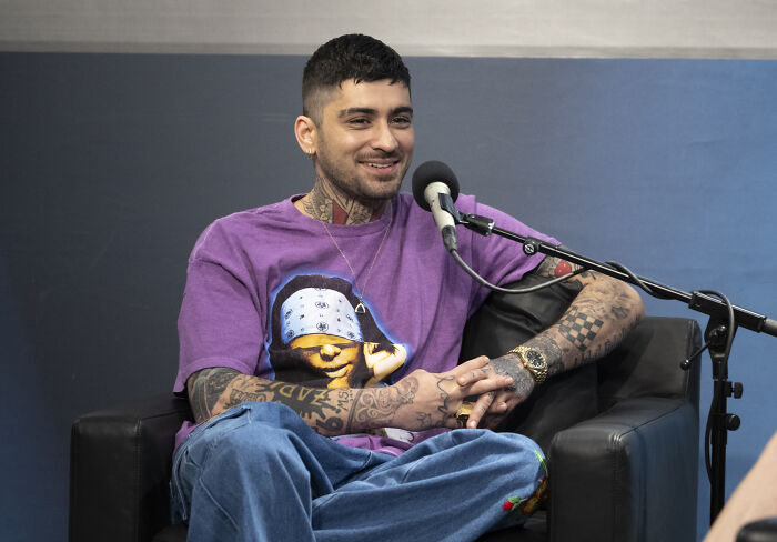 Former band member with tattoos and earrings, wearing a purple graphic tee, sitting and smiling during an interview session.