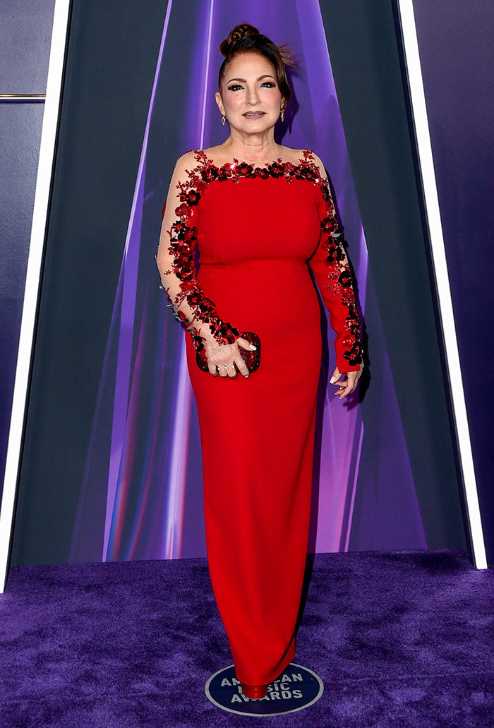 Woman in a red embellished gown posing on the purple carpet at the 2025 American Music Awards worst dressed stars event.