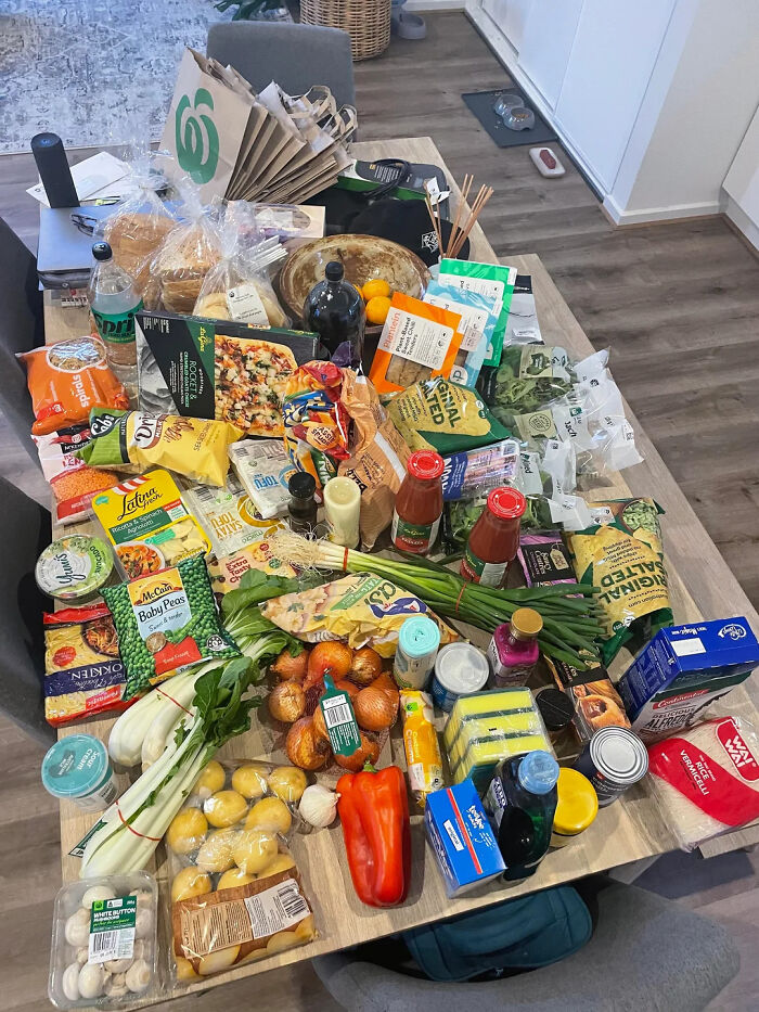 Grocery store haul with various fresh vegetables, snacks, drinks, and pantry staples on a wooden table.