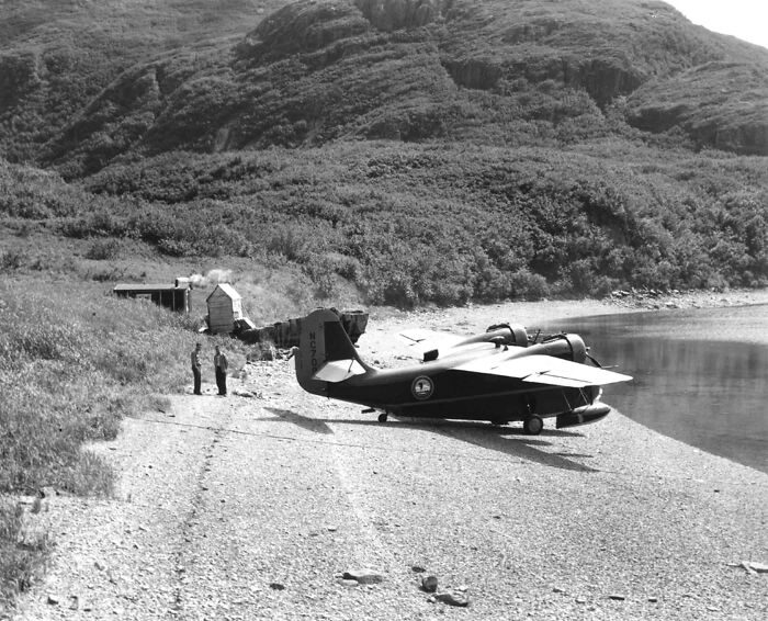 Seaplane landed on a remote shore with two people nearby, showcasing historic commutes in a bygone working world.