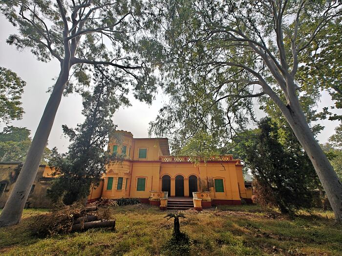 Historic yellow mansion surrounded by tall trees and greenery, representing Simultala as a timeless escape from the modern world.
