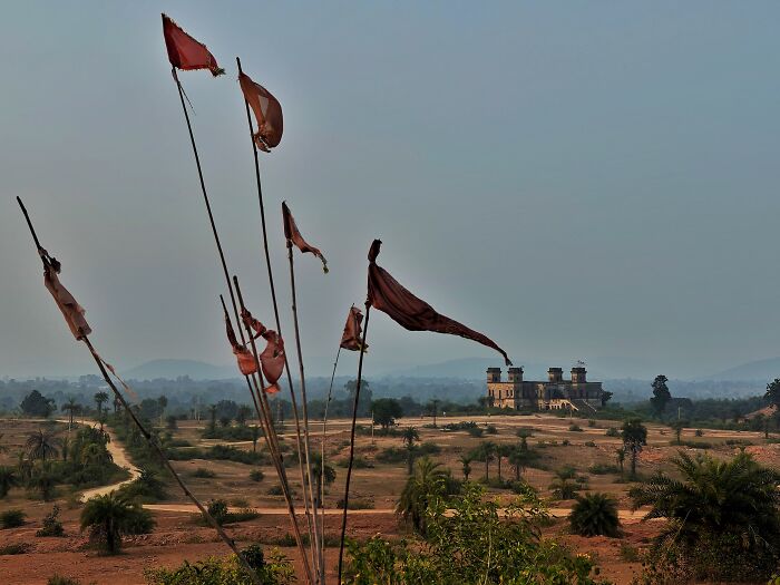 Fading red flags in foreground with a historic fort in Simultala surrounded by dry landscape and distant hills.