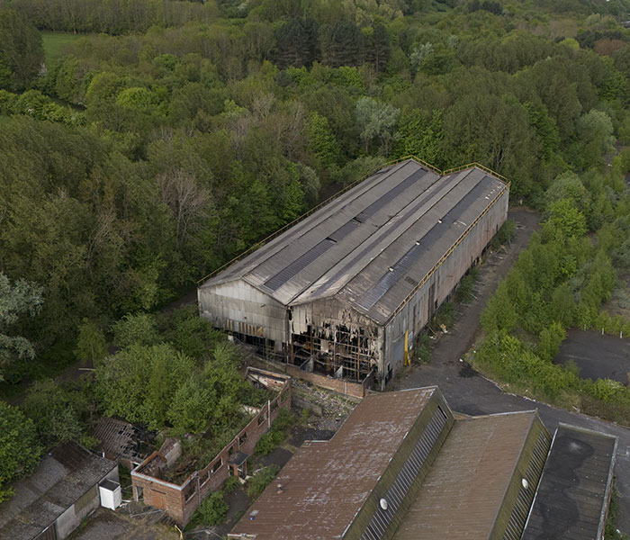 Aerial view of an industrial park building damaged by fire surrounded by dense green trees and vegetation. Aerial view of an industrial park building damaged by fire surrounded by dense green trees and vegetation.