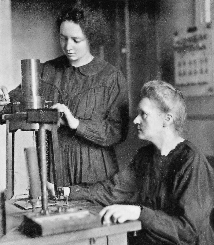 Marie Curie working with a female colleague in a vintage lab setting, showcasing early scientific research equipment.