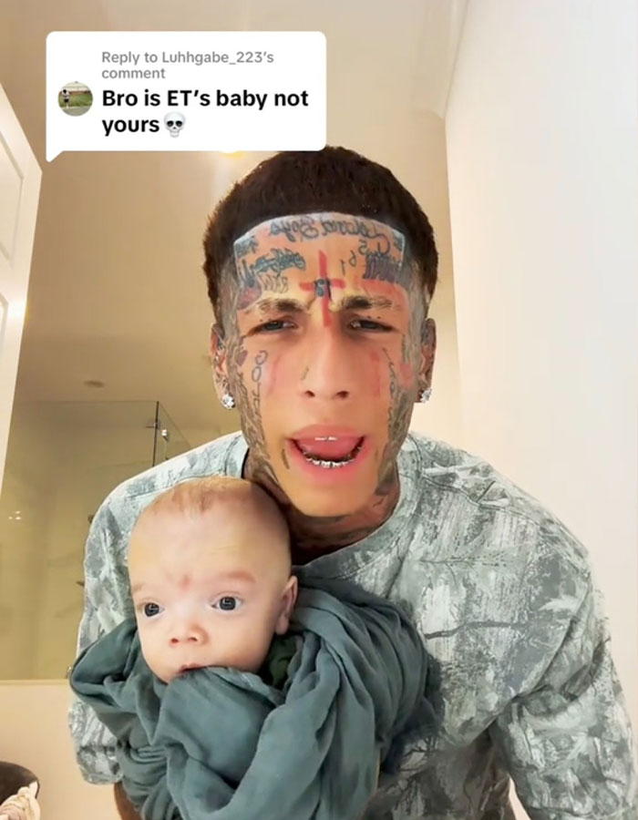 Island Boy with extensive face tattoos holding ET's baby wrapped in a blanket, addressing fans in a video.