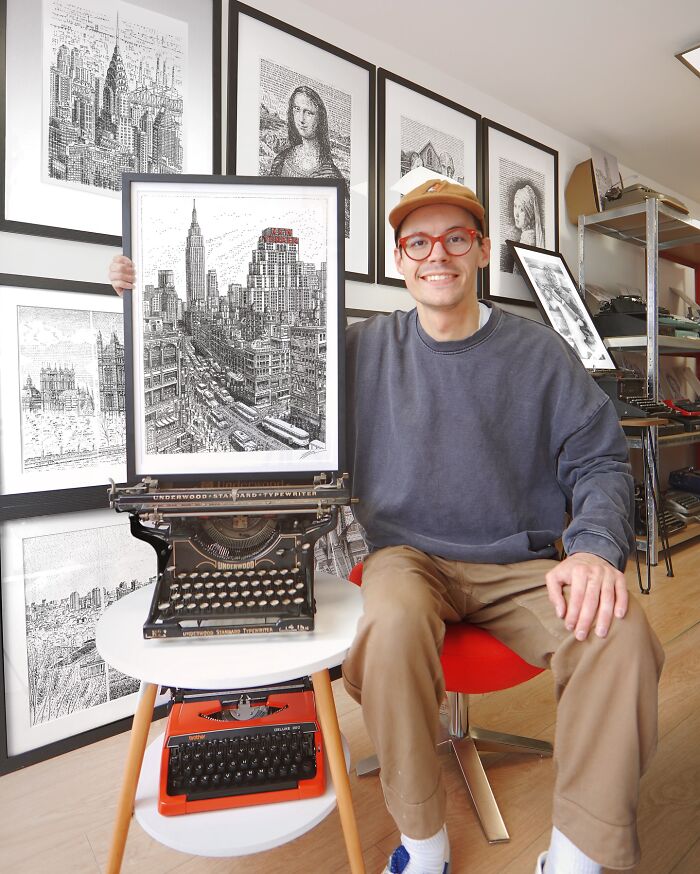 Young artist sitting with detailed typewriter drawing, surrounded by framed typewriter art in studio.