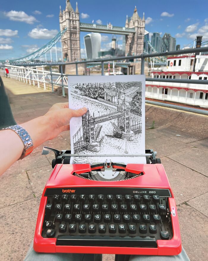 Hand holding detailed typewriter drawing of Tower Bridge with a red typewriter and actual Tower Bridge in the background.