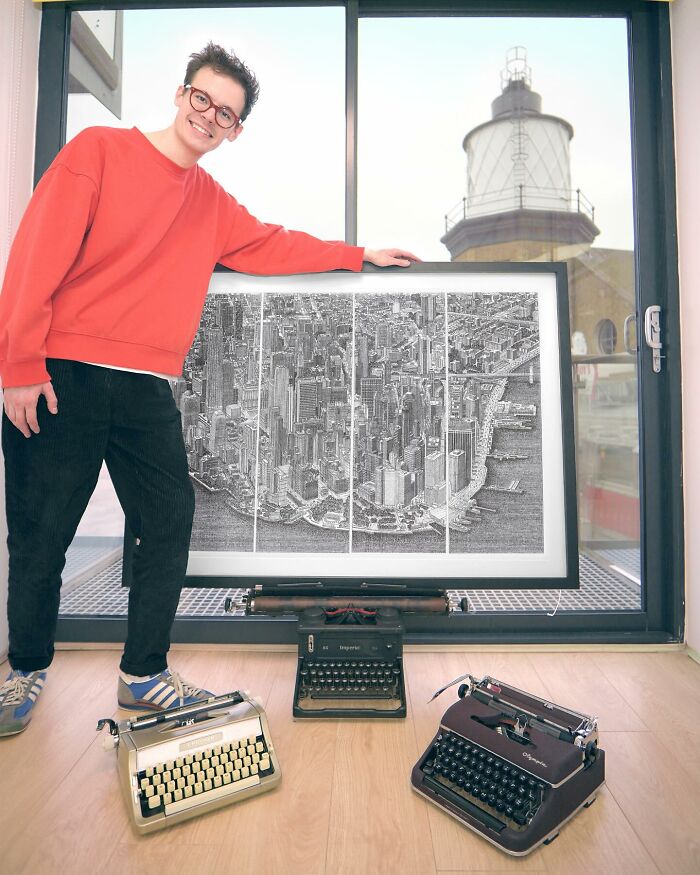 Young artist stands by detailed cityscape drawing created with a typewriter, surrounded by vintage typewriters on the floor.