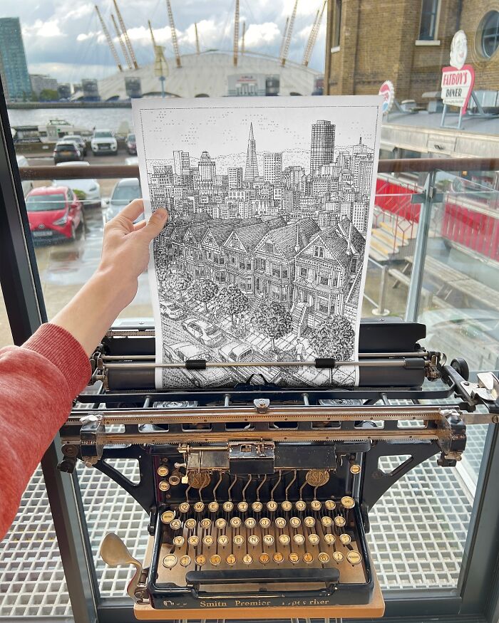 Hand holding a detailed typewriter drawing of cityscape and houses, showcasing young artist's intricate typewriter art.