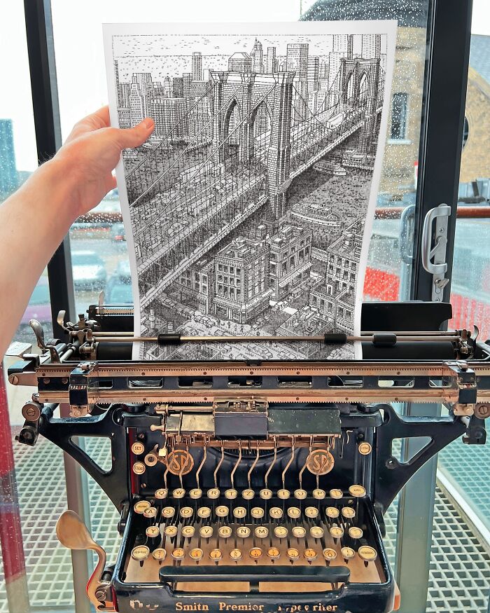 Hand holding detailed cityscape drawing created with a typewriter, placed on an antique Smith Premier typewriter.