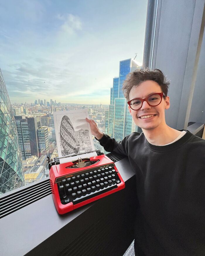 Young artist smiling beside a red typewriter, holding impressively detailed cityscape drawing created with typewriter keys.