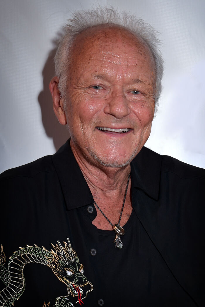 Elderly man smiling, wearing black shirt with dragon embroidery and necklace, representing notable people who passed away in 2025.