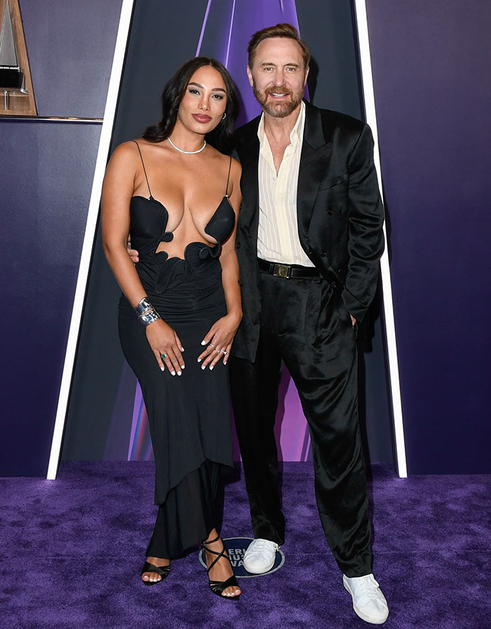 Couple posing on purple carpet wearing bold outfits, featured among worst dressed stars at 2025 American Music Awards.