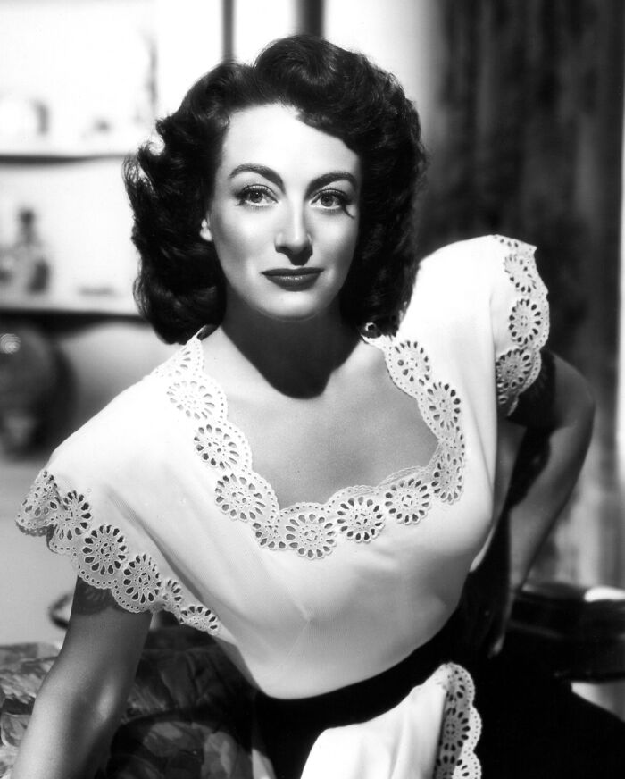 Black and white portrait of a glamorous 1940s Hollywood icon wearing a detailed white dress with lace trim.